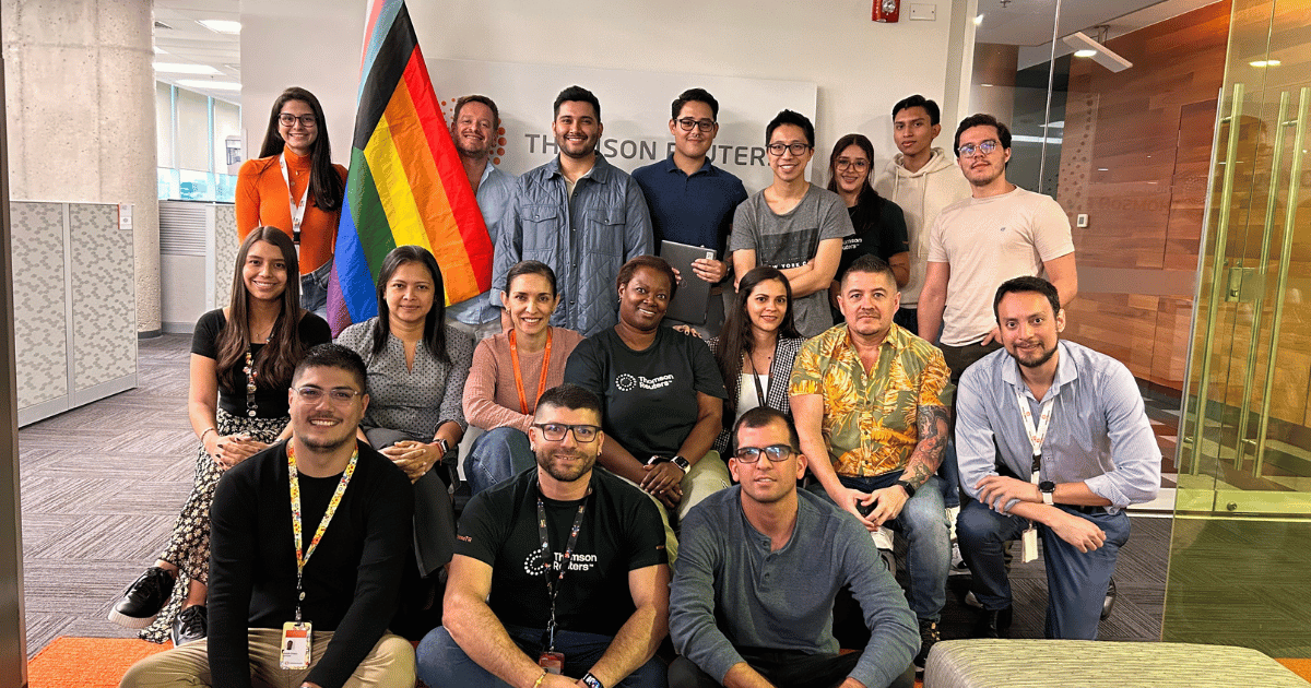 A large group of people pose for a photo together holding the Pride flag. 