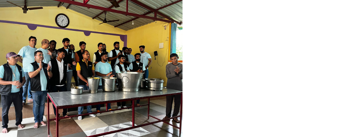 A large group of people stand together during a volunteer event. There is a table with large buckets in front of them.